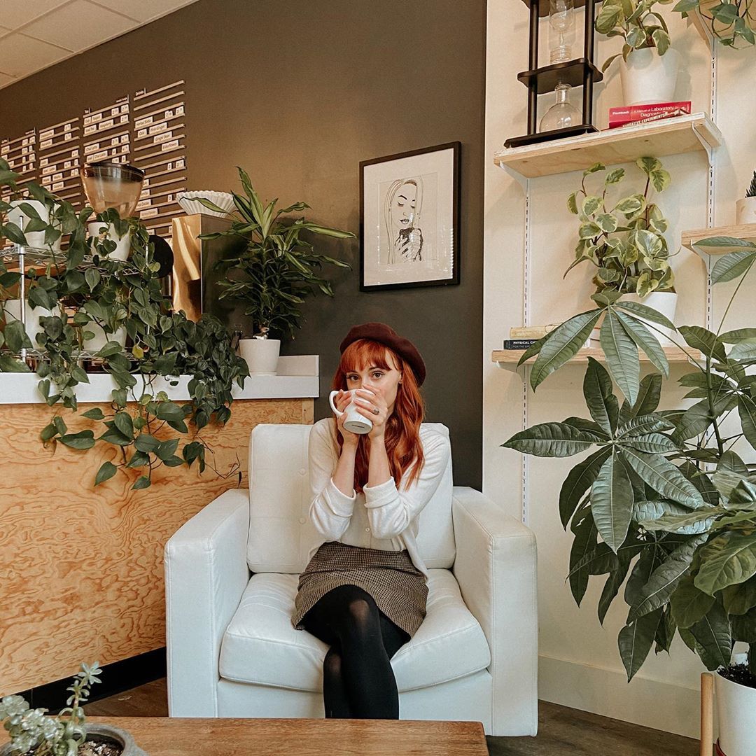 A patron sits in a comfy armchair, drinking coffee surrounded by plants.